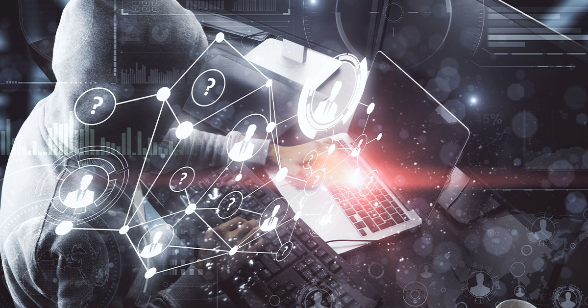 A person in a hoodie sits at a desk, working on a laptop with concentration.