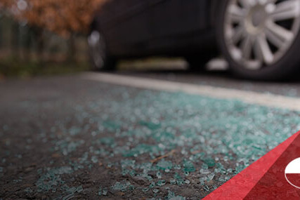 Shattered car window glass on pavement beside a parked car.