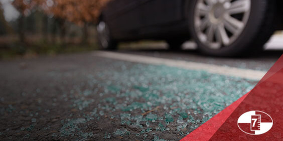 Shattered car window glass on pavement beside a parked car.