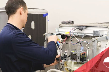 Technician repairing the internal wiring of a machine with the front panel open.