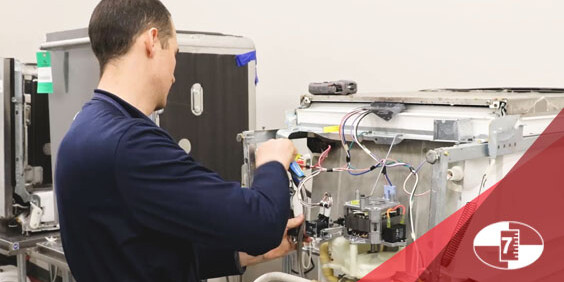 Technician repairing the internal wiring of a machine with the front panel open.