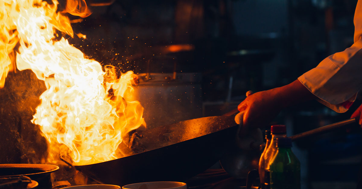 A chef skillfully cooks in a wok over an open flame, showcasing vibrant ingredients and intense heat.