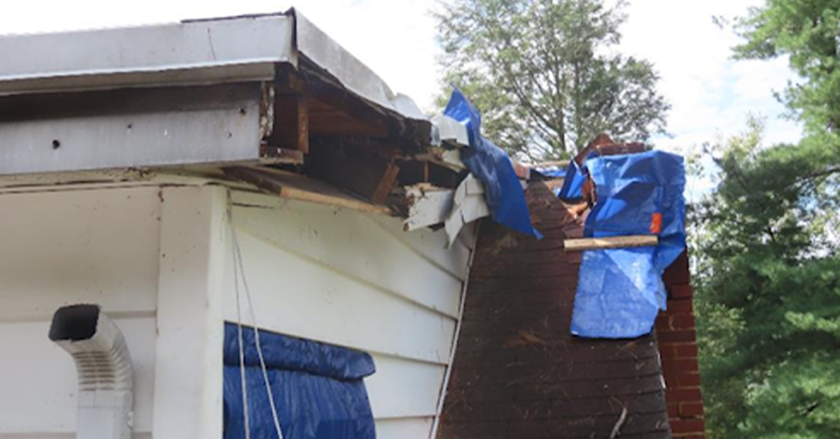 A house with a blue tarp on the roof, indicating ongoing roof repairs.