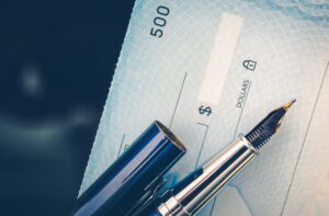 Close-up of a check with a ballpoint pen resting on it.