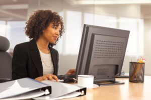 A woman seated at a desk, focused on her computer screen while typing.