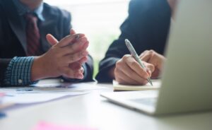 Two business individuals sitting together at a table, focused on a laptop in front of them.