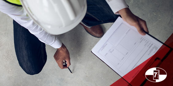 A man wearing a hard hat and safety vest holds a clipboard, standing in a construction environment.
