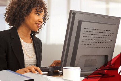 A woman seated at a desk, focused on her computer screen while typing.