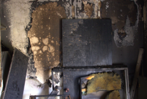 Burned room interior with charred walls and a door and window frames leaning against a wall.