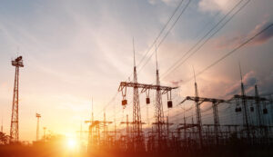 A vibrant sunset illuminates a power plant, highlighting the electrical towers